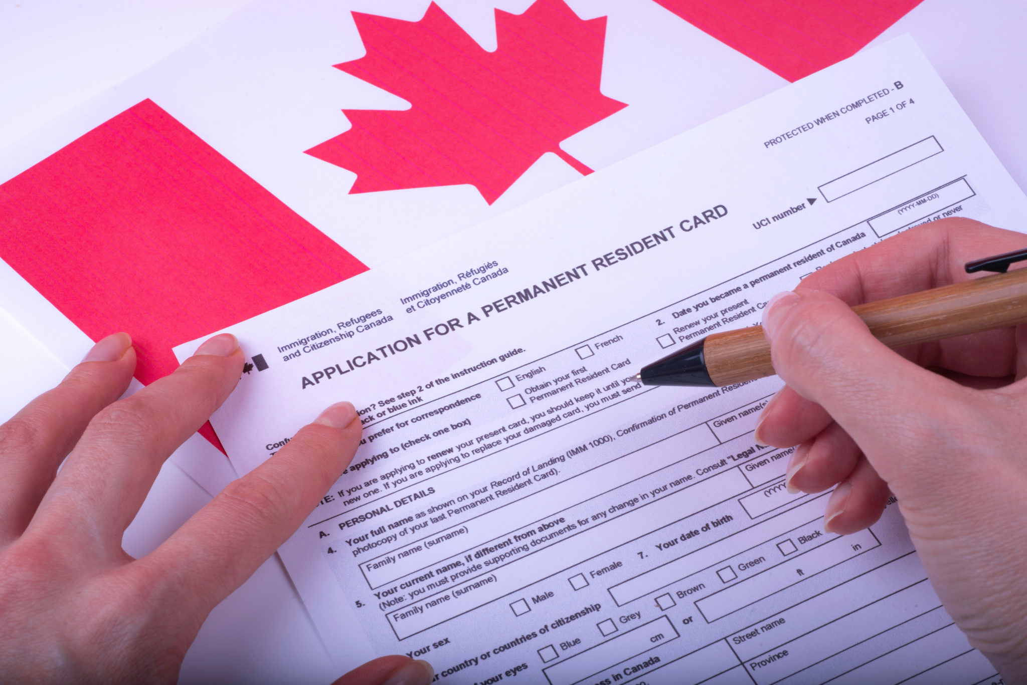Hands filling out Canadian immigration application form with maple leaf flag in background